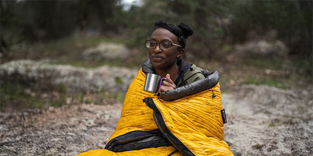 a women wrapped around a yellow and charcoal down sleeping quilt