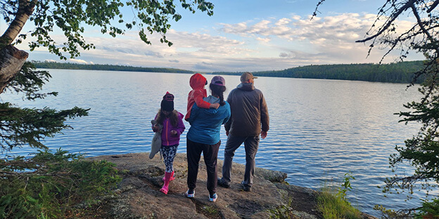 a family looking out on to a lake standing on a boulder