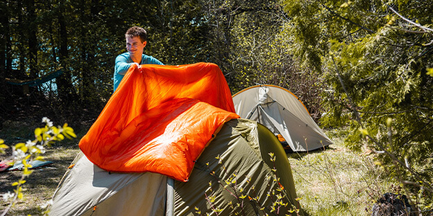 a man putting his orange synthetic enlightened equipment quilt on top of his tent