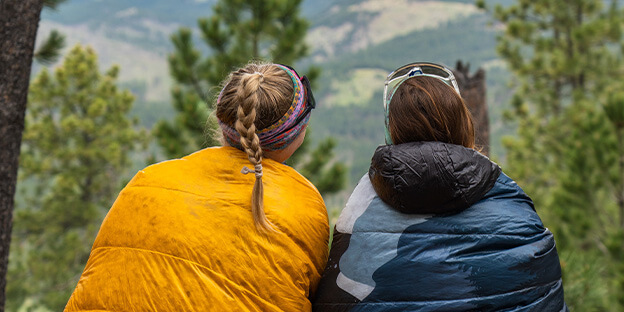 2 women wrapped around their yellow and navy blue quilts looking at a vie of the SHT