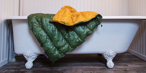 a photo of a green and yellow sleeping quilt hung over a bathrop ready to be washed