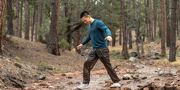 a man walking on a trail wearing charcoal enlightened equipment copperfield wind pants